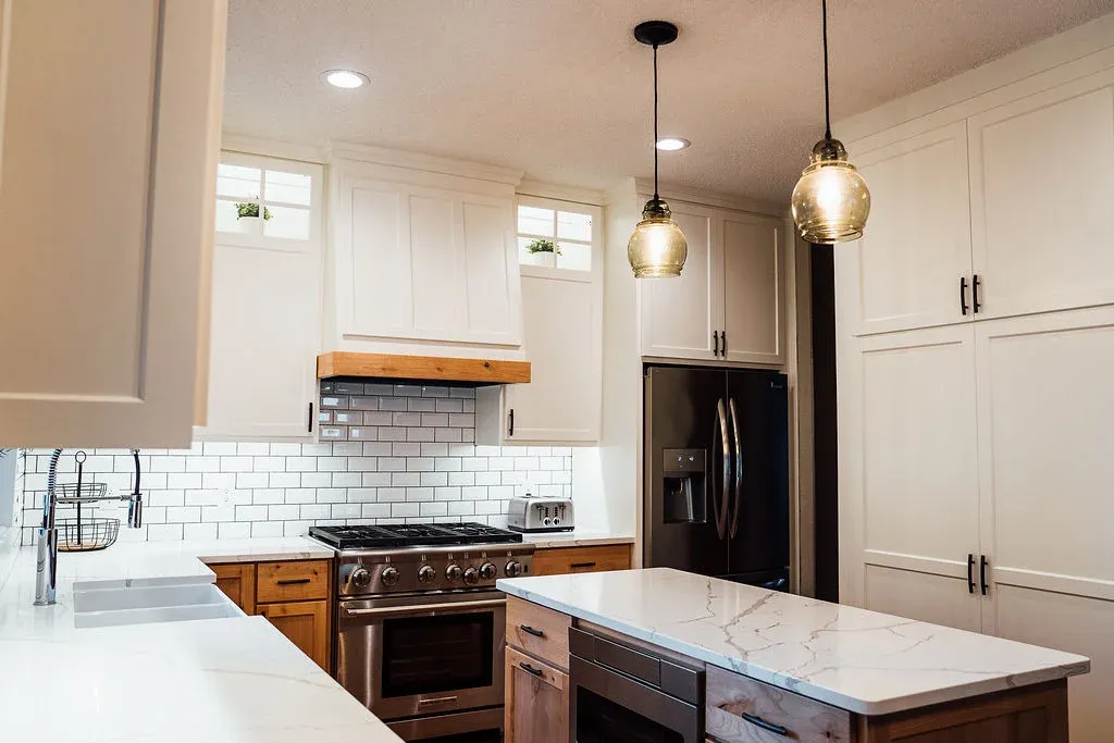 Stained alder cabinetry with painted uppers, quartz countertops, and reflective subway tile in Lakeville kitchen remodel