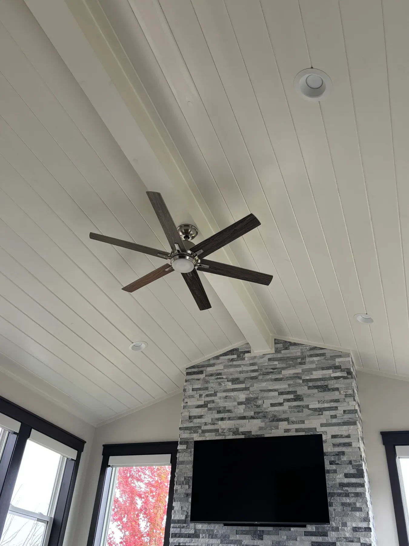 Painted tongue-and-groove vaulted ceiling with a ceiling fan above the stone fireplace in the Lakeville porch
