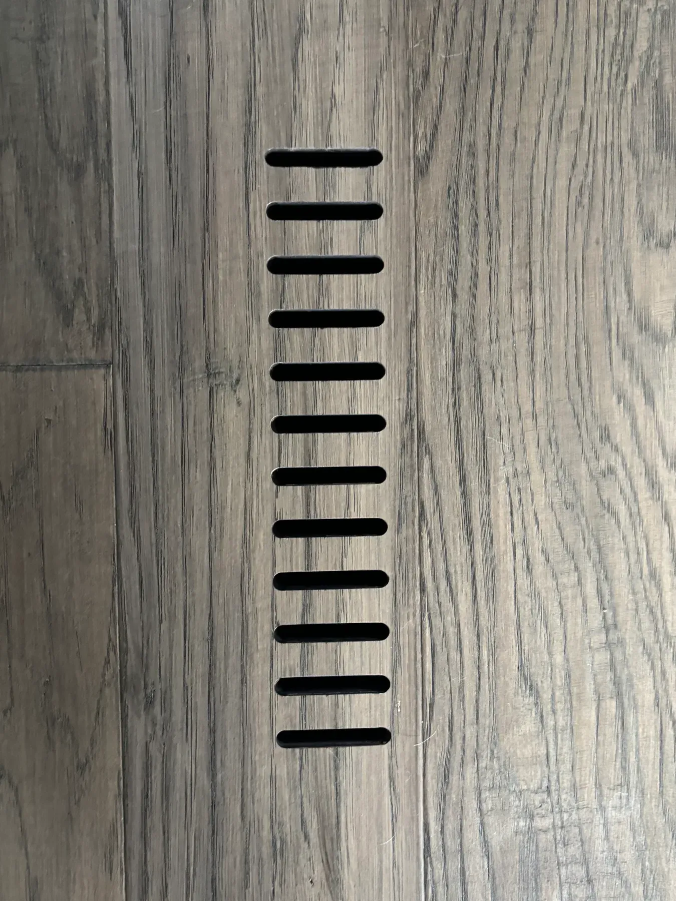 Floor vent built into matching luxury vinyl plank flooring at the entry to the Lakeville porch