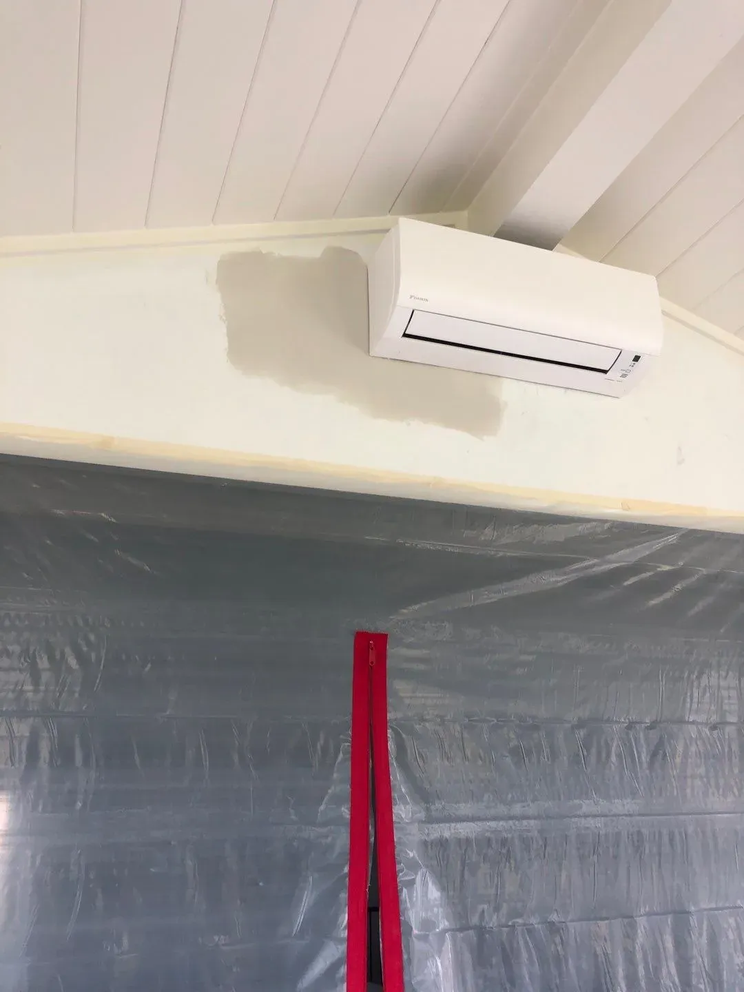Zippered plastic dust wall over the doorway into the house, with the ductless unit mounted above, during the Lakeville porch build
