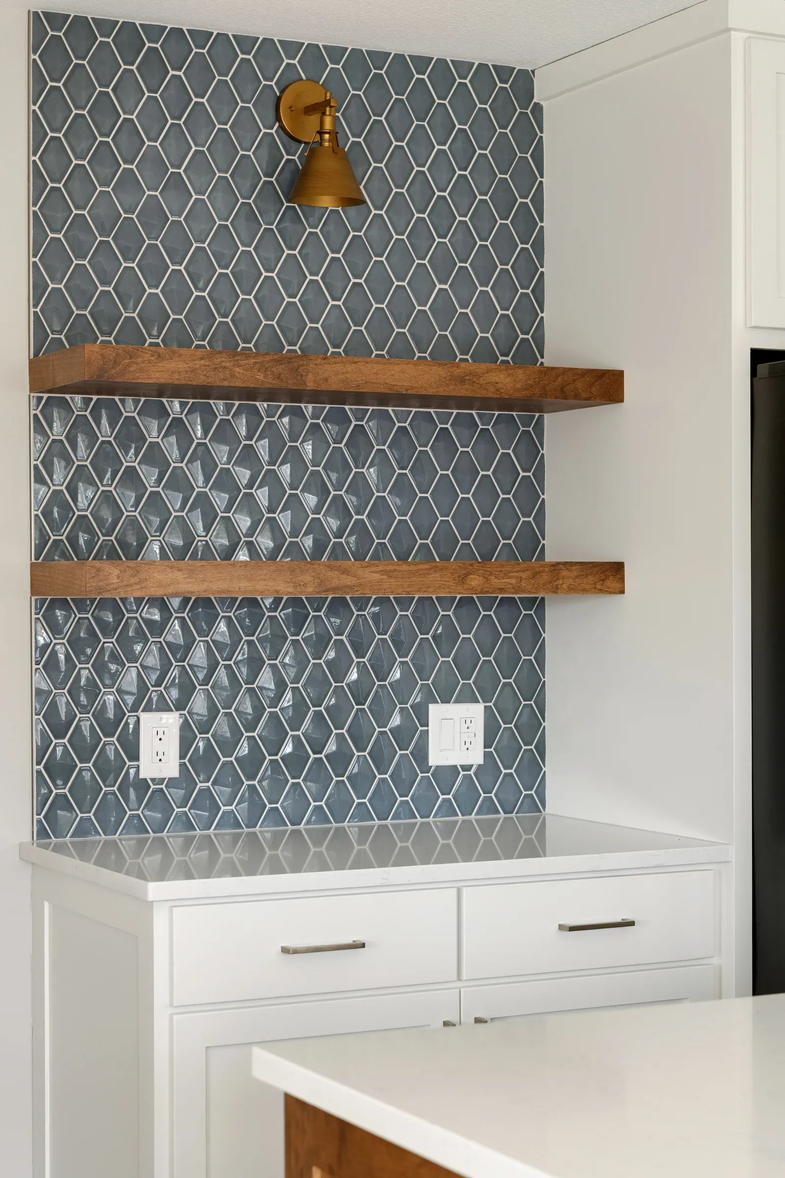 Close-up of blue-green geometric tile backsplash with brass wall sconce and open wood shelving in Elko New Market kitchen