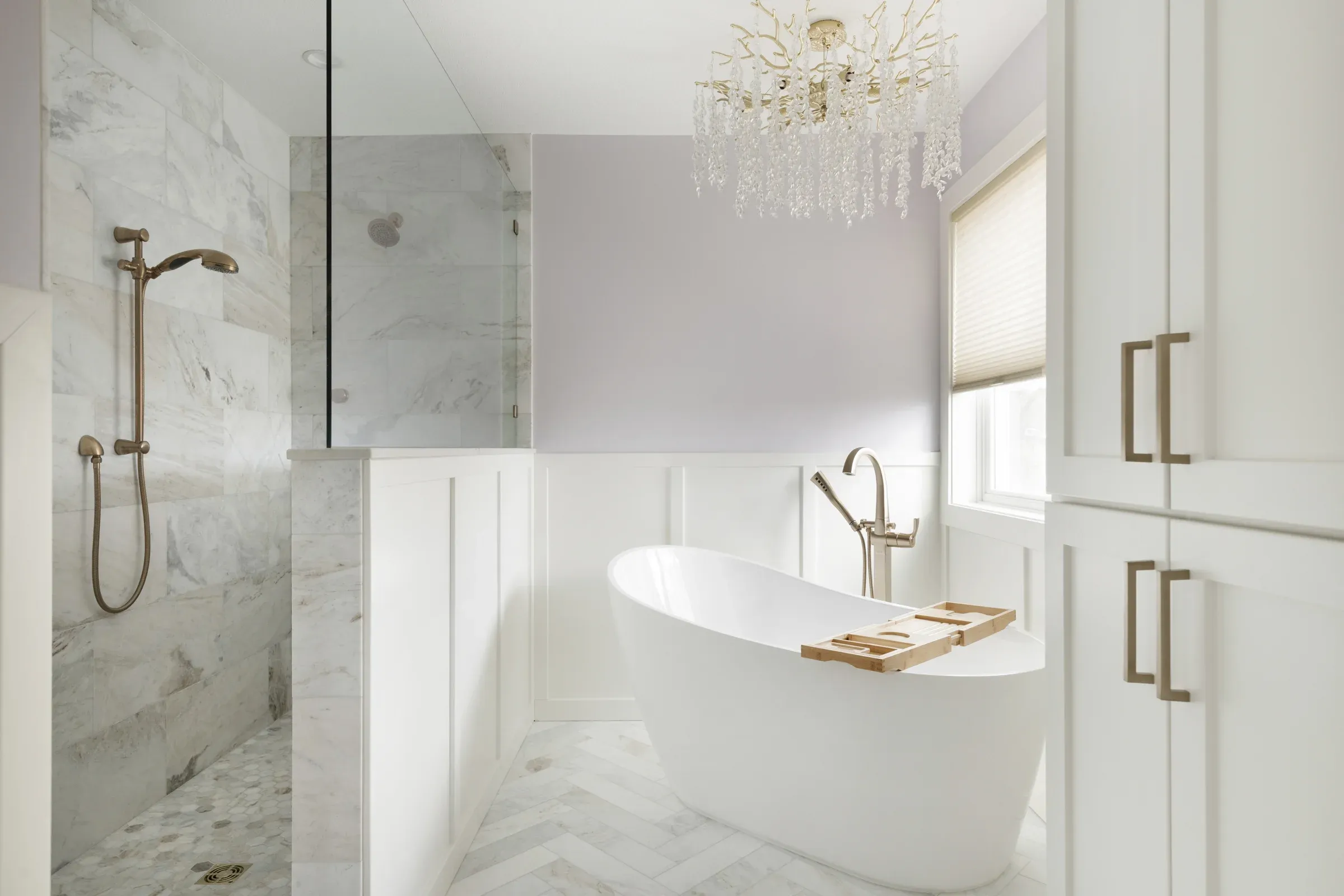 Walk-in marble shower and freestanding soaking tub in Elko New Market primary bathroom remodel – brass fixtures, wainscoting, and crystal chandelier by Honey-Doers Remodeling