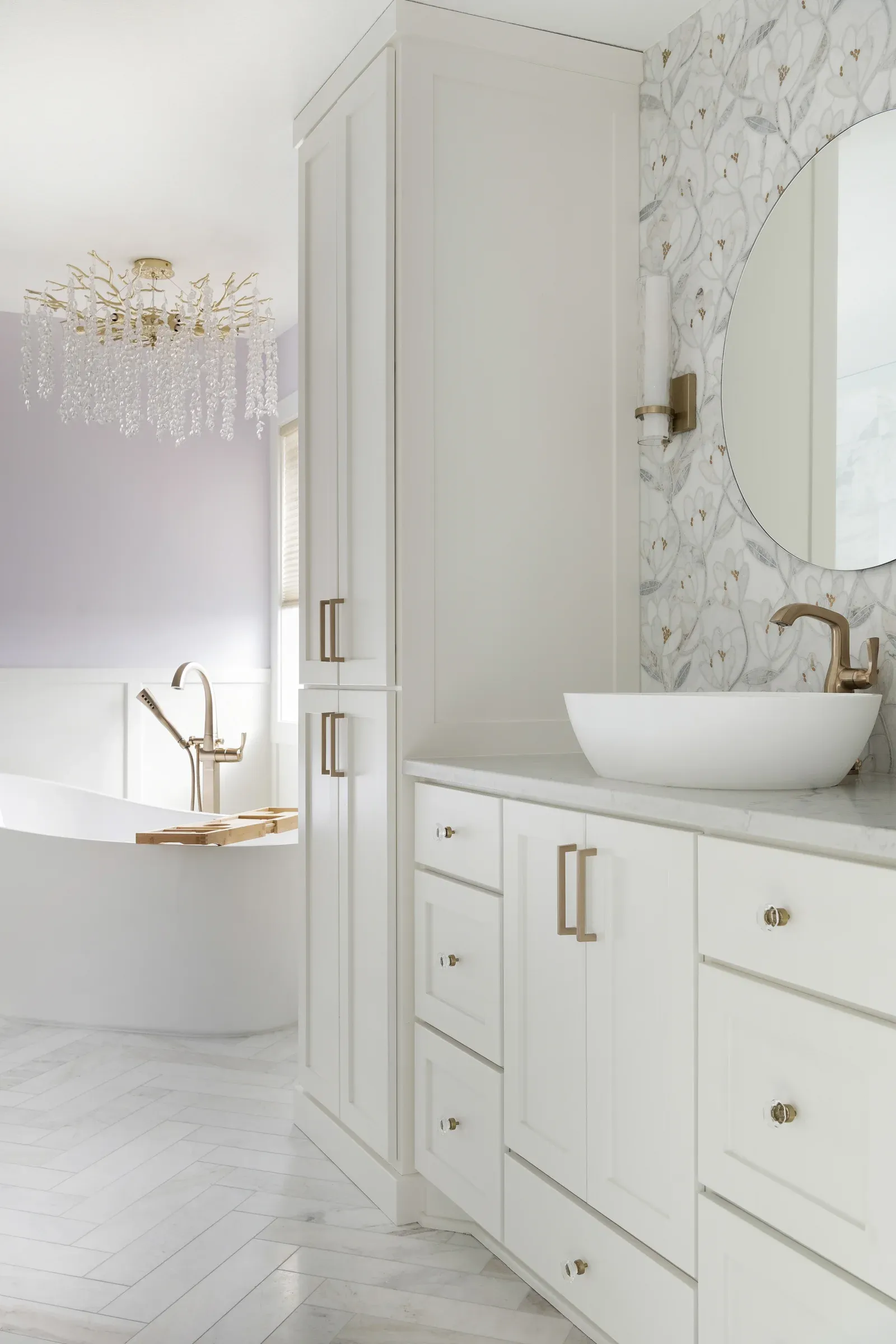 White vanity cabinetry with tall linen tower, vessel sink, floral mosaic tile backsplash, and round mirror – Elko New Market primary bathroom by Honey-Doers Remodeling