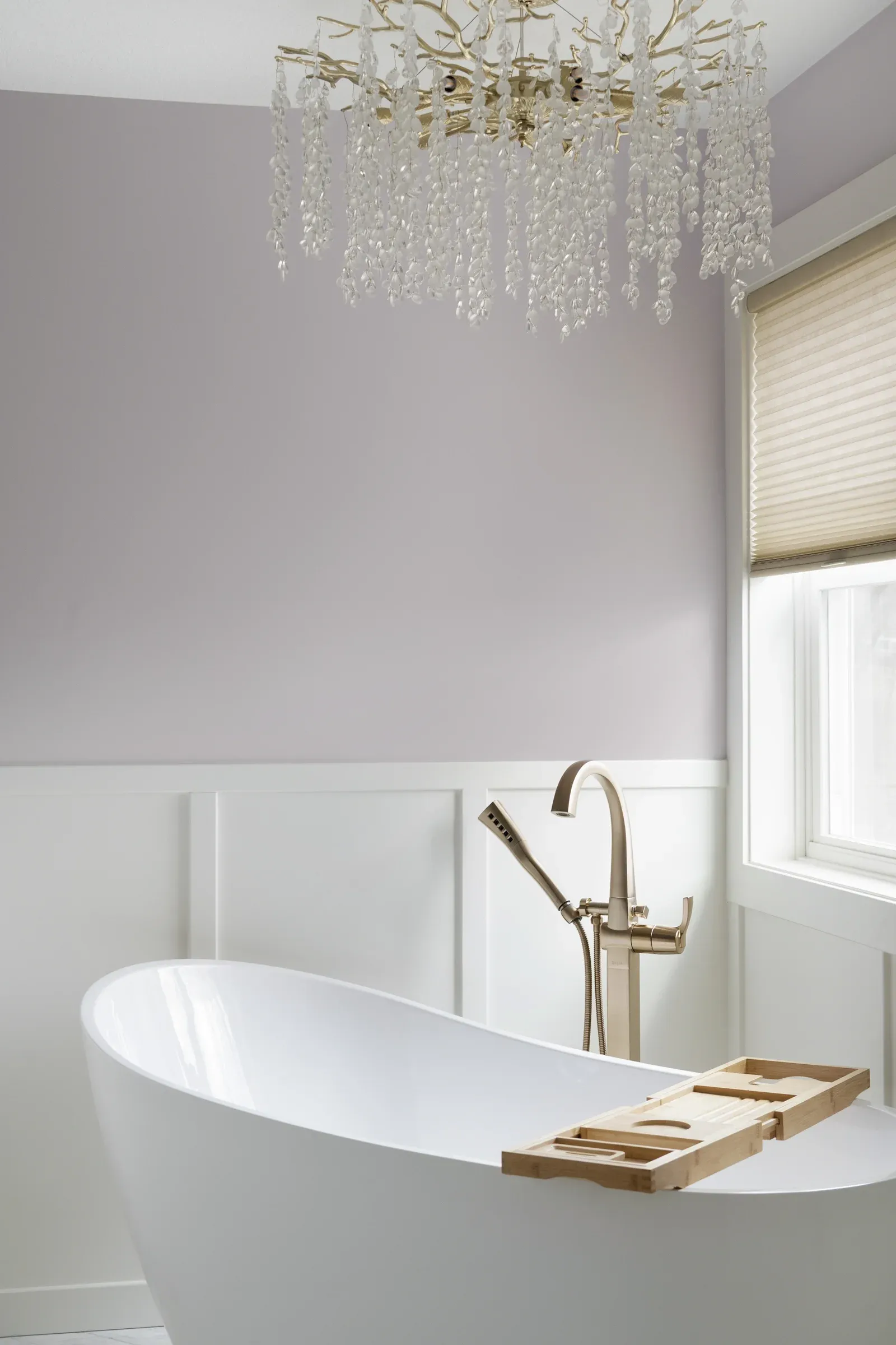 Crystal chandelier over freestanding soaking tub with lavender accent wall and champagne bronze tub filler – Elko New Market primary bathroom remodel by Honey-Doers Remodeling