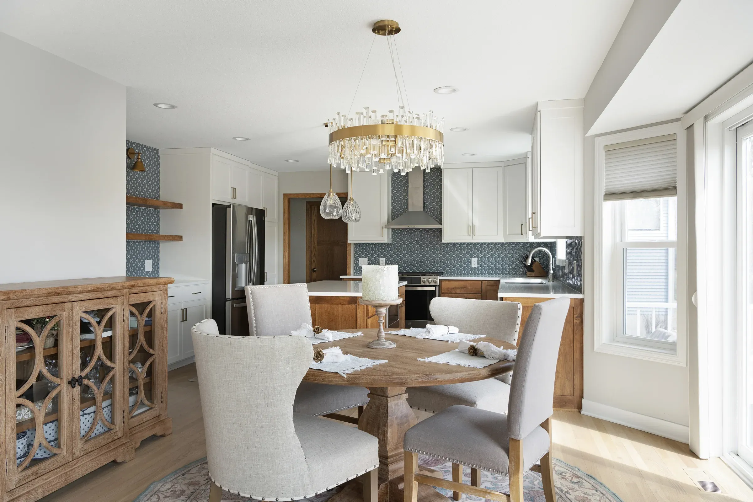 Dining area with brass crystal chandelier, round table, and remodeled kitchen visible beyond – Elko New Market main-level remodel by Honey-Doers