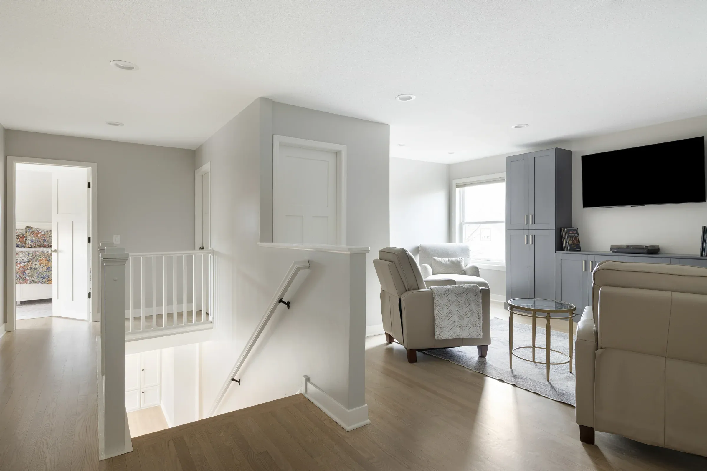Second-floor landing and entertainment area after refresh in Elko New Market MN – white railing, hardwood floors, blue-gray cabinet unit, and wall-mounted TV by Honey-Doers Remodeling