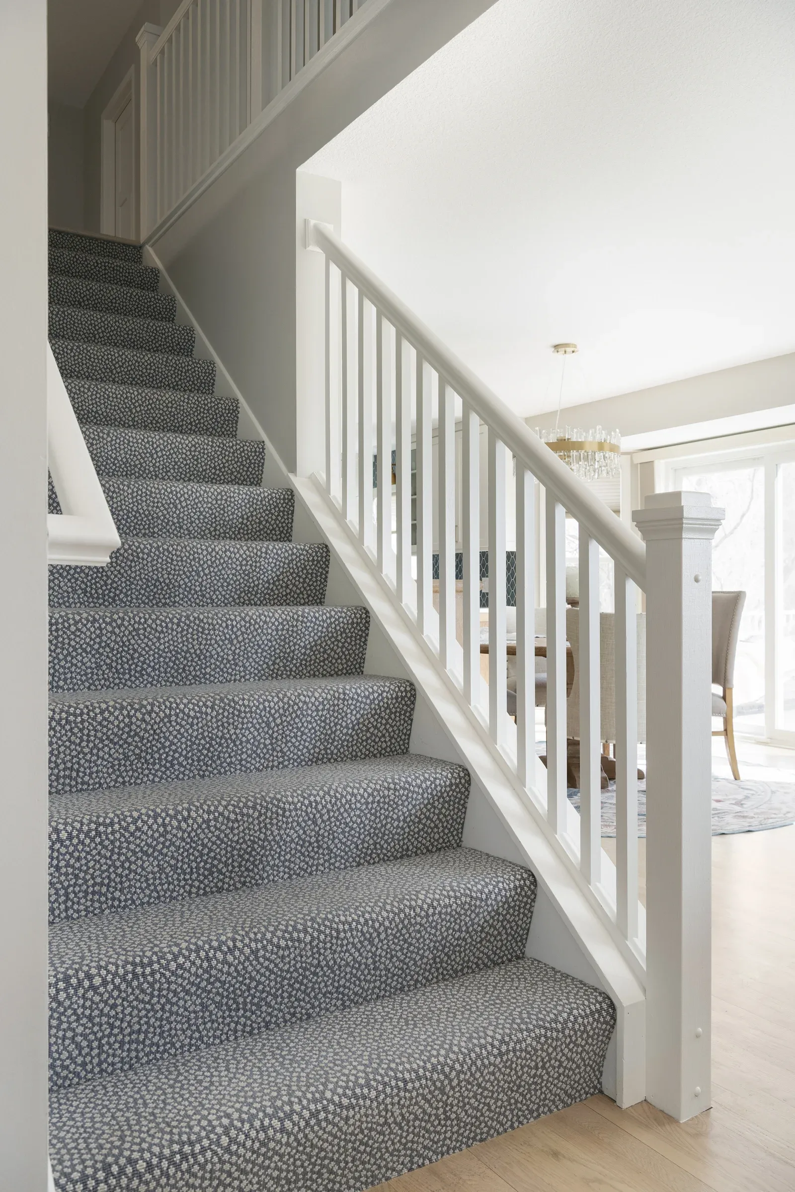 Staircase with patterned blue-gray carpet, white painted railing and trim, and view to remodeled main level – Elko New Market whole-home remodel by Honey-Doers Remodeling