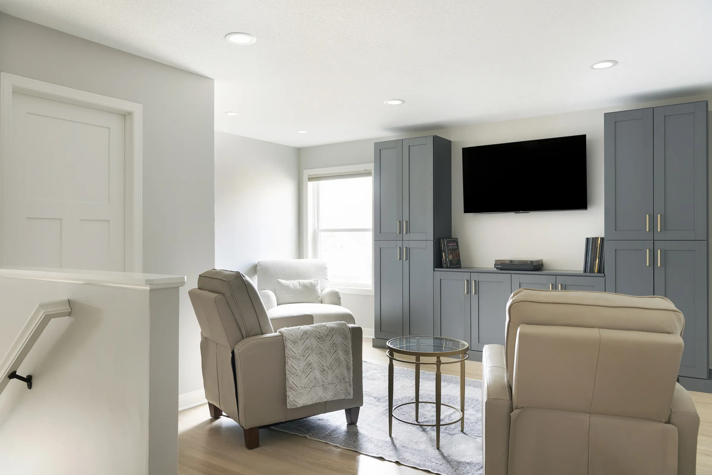 Upper-level entertainment and home office area with blue-gray semi-custom cabinet unit, wall-mounted TV, hardwood floors, and recliner seating – Elko New Market MN by Honey-Doers Remodeling