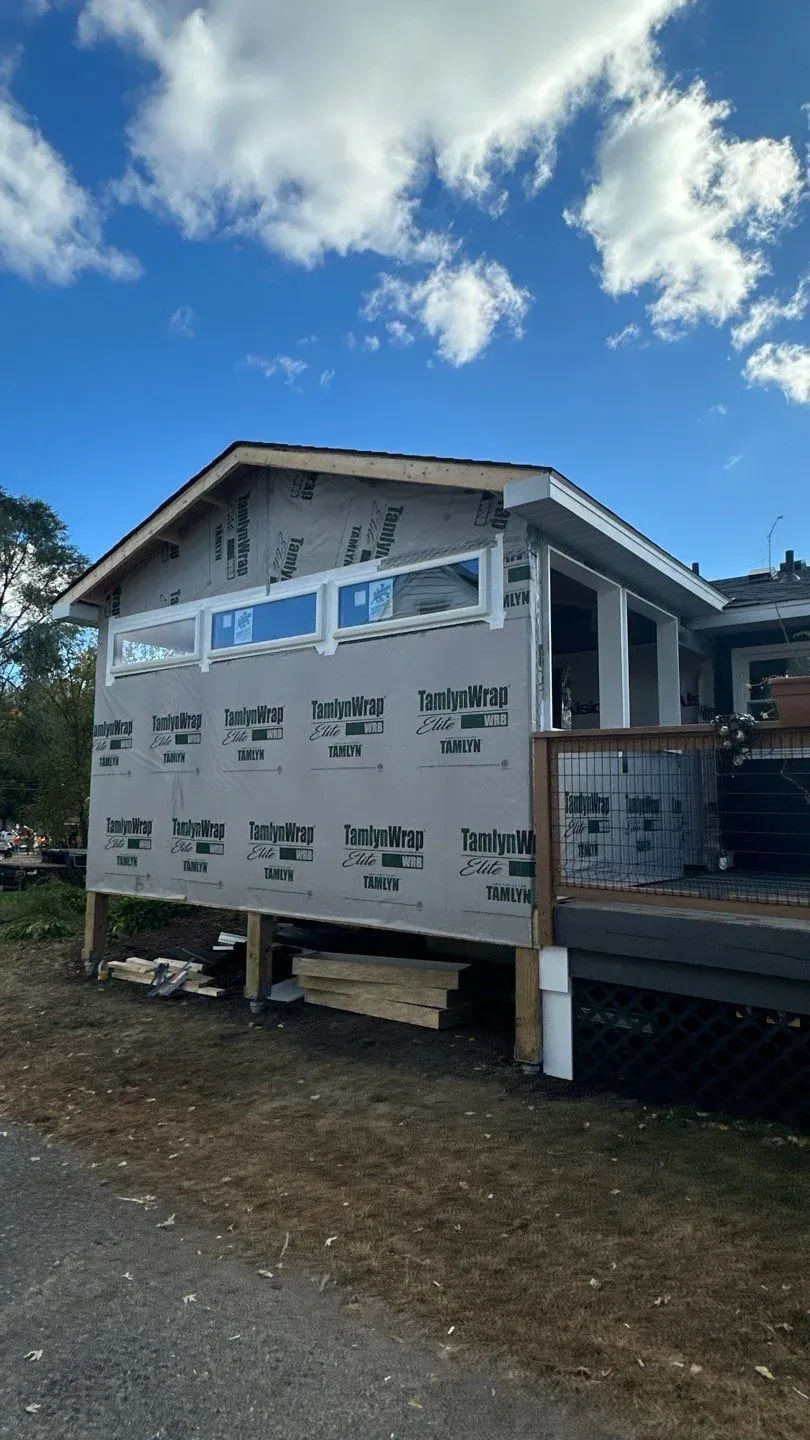 A three-season porch addition in Minneapolis framed and wrapped in house wrap, standing on posts set on footings beside an existing deck