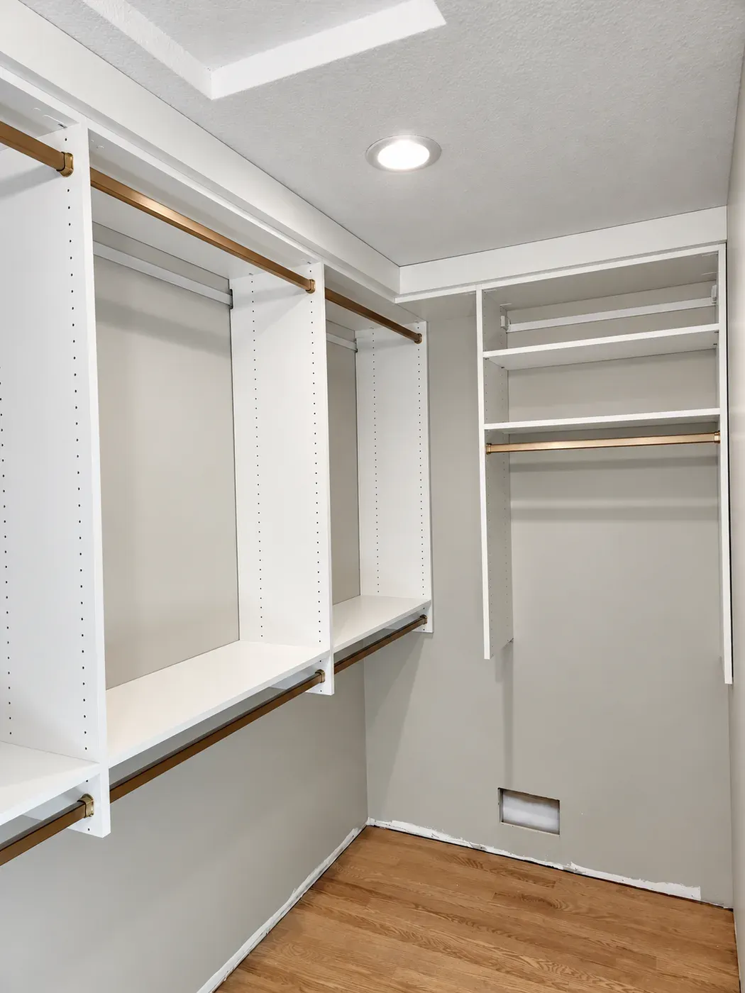 Double-hang rods with brass-finish bars along one wall of a small walk-in closet in Elko New Market, and a shelf-and-rod unit on the end wall