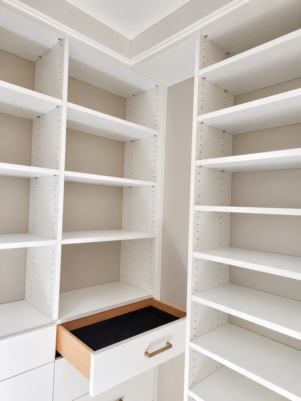 Shelf towers on two walls of an Elko New Market closet, with a lined pull-out drawer at the base