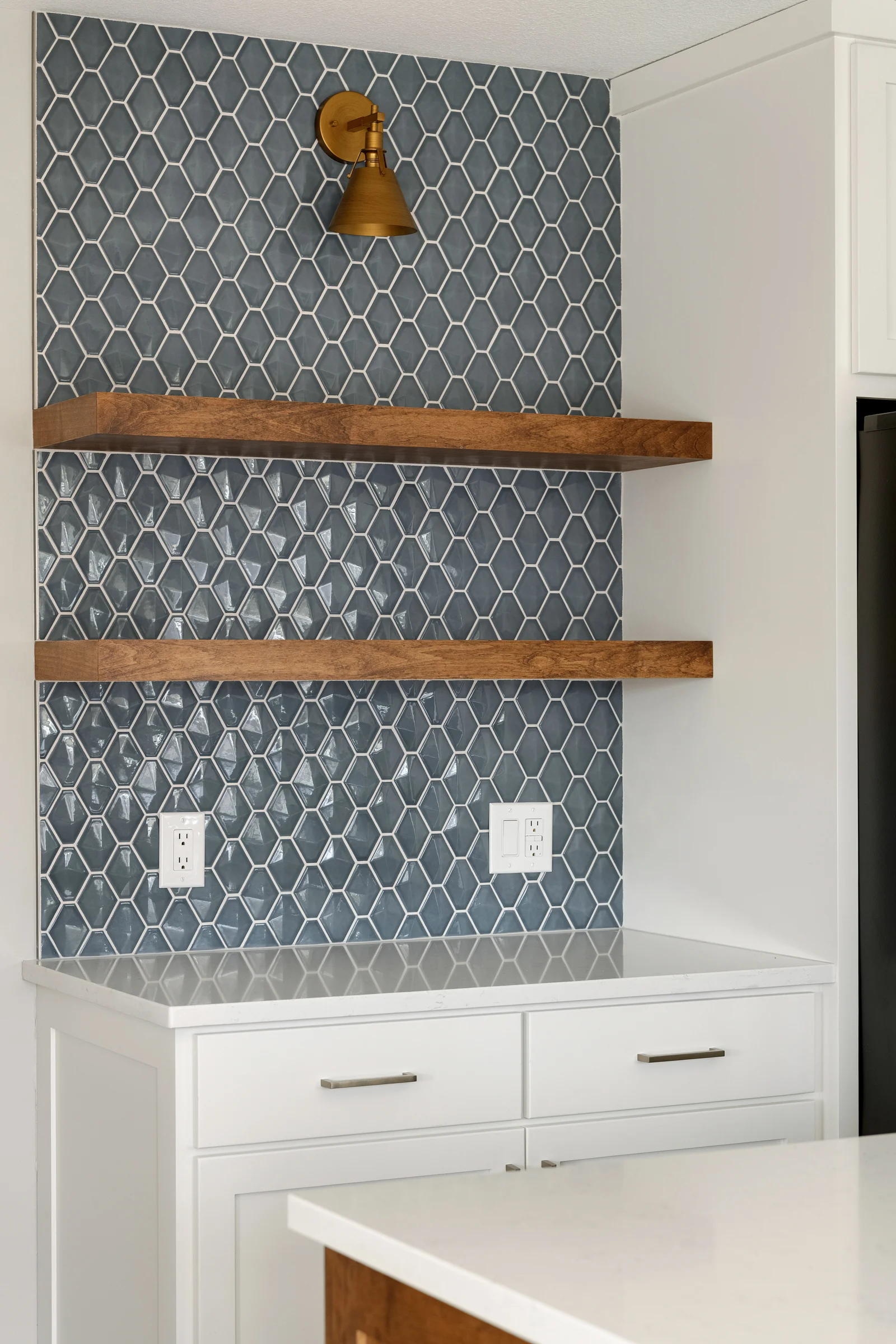 Close-up of blue-green geometric tile backsplash with brass wall sconce and open wood shelving in Elko New Market kitchen