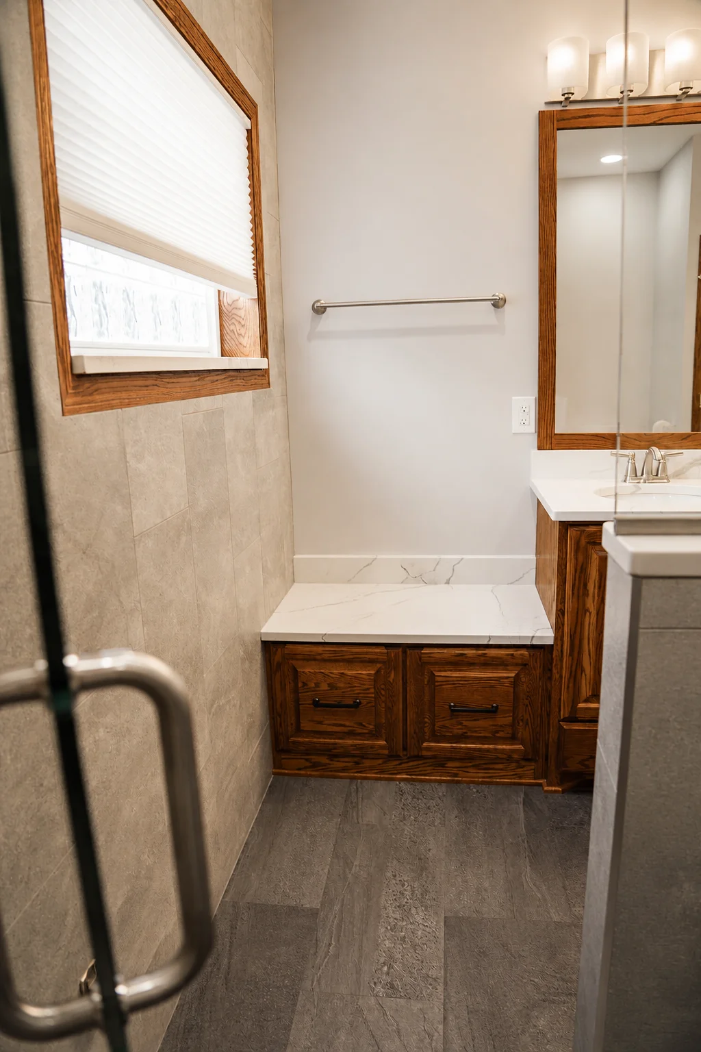 Quartz-topped storage bench beside custom oak double vanity in Rosemount primary bathroom remodel